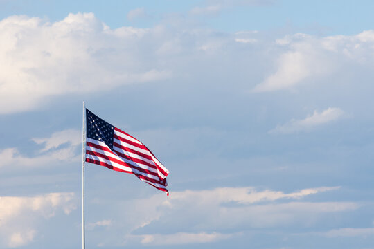Horizontal image of the American Flag  Against a sky with thick white and gray cumulus clouds and blue sky. Flag is unfurled in the breeze.