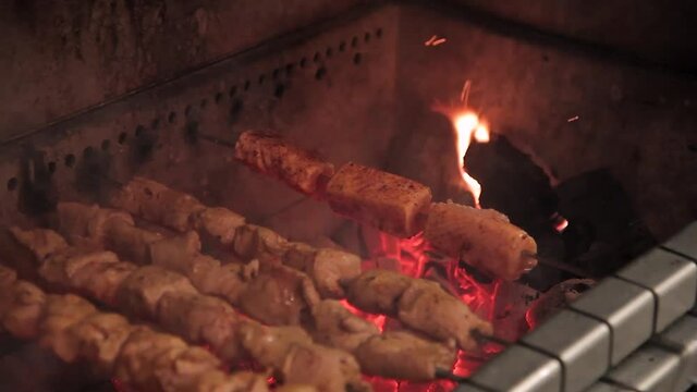 The shish kebab slowly turns on fire in an automatic barbecue. Pieces of meat on a skewer spinning in a shish kebab without the participation of a chef. Juicy parts are fried in a barbecue on metal