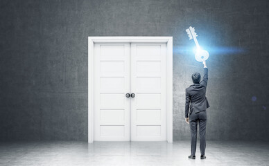 Businessman holding a giant key near large door