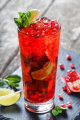Fresh red lemonade with mint, pomegranate, lime and ice in glass on wooden background. Summer drinks and cocktails