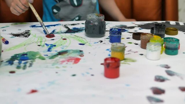 The boy draws paints in the house at the table.