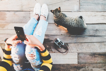 Hipster lifestyle - Girl in jeans with black smartphone and retro camera with cat sit on the wooden floor. vintage film color effect and retro color style