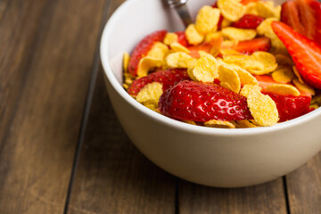Corn flakes with fresh strawberry in bowl on the rustic background. Shallow depth of field.