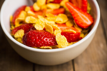 Corn flakes with fresh strawberry in bowl on the rustic background. Shallow depth of field.