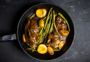 Grilled pork with asparagus and peaches in pan on the black background. Shallow depth of field.