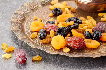 Various dried fruits on toreutic plate over stone background