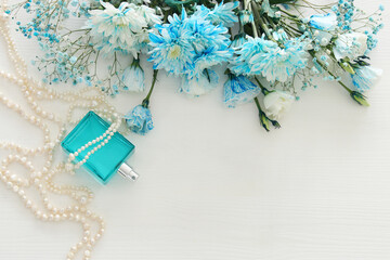 beautiful and delicate blue flowers arrangement next to pearls necklace and fresh perfume