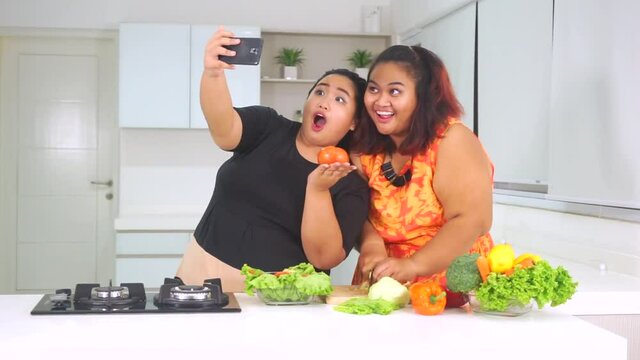 Video footage of two young overweight women making salad and taking selfie photo together with a smartphone in the kitchen