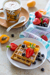 Background breakfast. A cup of cappuccino coffee and Belgian waffles with berries on the kitchen table.