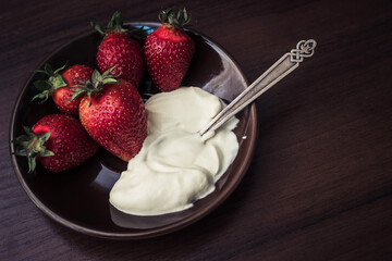 Strawberries with a spoon of cream on a plate