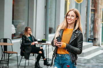 Fototapeta na wymiar attractive young stylish woman holding a cup of coffee and standing near cafe. concept of lifestyle fashion free time walking people