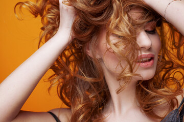 Fototapeta premium Happy beautiful redheaded girl with luxurious curly hair. Studio portrait on yellow background. Excellent hair