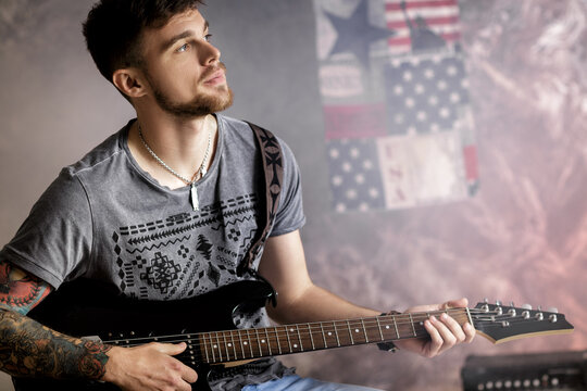 Young handsome musician playing electric guitar on dark background