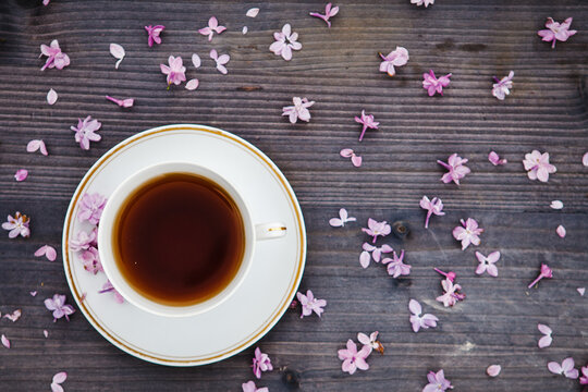 A cup of tea on a wood background with lilac flowers