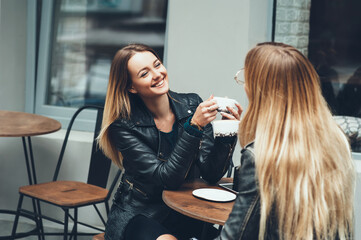 Two beautiful young women in fashion clothes having rest talking and drinking coffee in restaurant outdoor. concept of friendship lifestyle fashion. sunny day for walk with friends and have a fun.