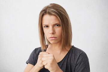 Aggressive young female keeping her fists ready to fight and defense herself against injustice or violence. Strong woman clenching fists as if boxing, looking at camera with serious expression