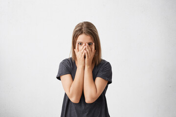 Stressed scared female student in casual t-shirt covering her face, feeling afraid of stressful examination at college. Ashamed teenage girl feeling frustrated, hiding herself behind palms. Horizontal