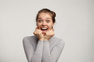 Portrait of emotional positive European teenage girl wearing her light hair in bun, shouting in...