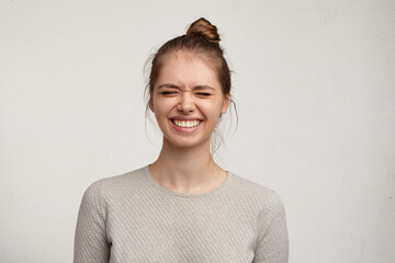 Headshot of gorgeous attractive young lady with hair gathered in bun smiling broadly and closing eyes, having impatient excited look, trying not to peep as her boyfriend preparing a surprise on her