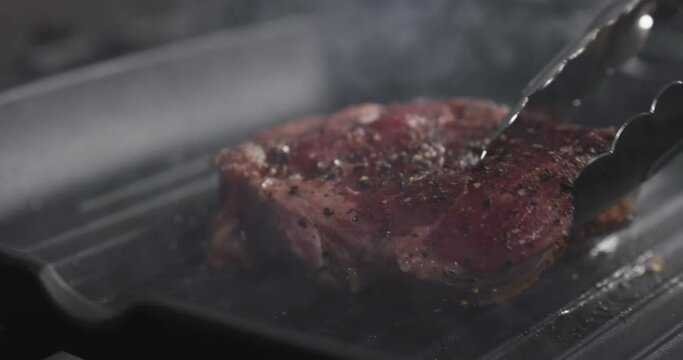 Slide slow motion shot of flip rib eye steak on grill pan, 4k 60fps prores footage