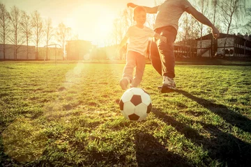 Poster Father and son playing together with ball in football under sun © Andrii IURLOV