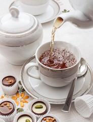A white cup of tea with a teaspoon and chocolate.