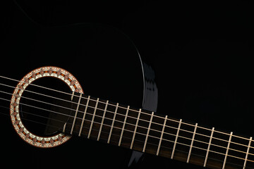 Plakat Part of a black Six-string classical acoustic guitar isolated on black background.