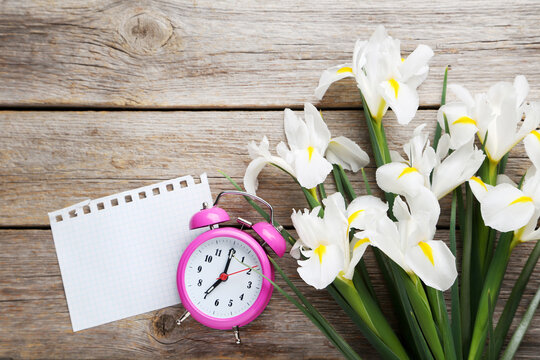 Bouquet of iris flowers with alarm clock on grey wooden table