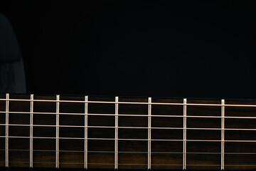 Part of a black Six-string classical acoustic guitar isolated on black background.