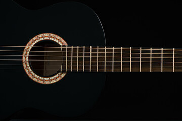 A black Six-string classical acoustic guitar isolated on black background.
