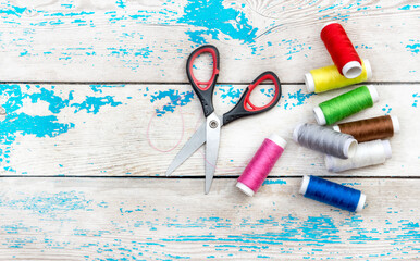 Scissors with colour sewing threads on a wooden background. Top view.