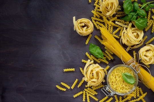 Various types of pasta with basil on a kitchen wooden table. The concept of Italian food. Top view, copy space.