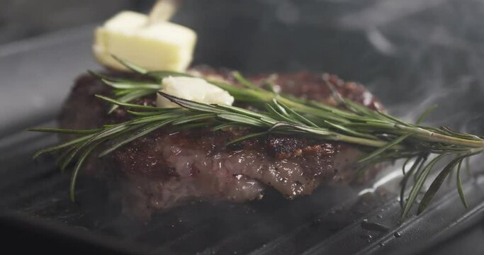 Slide slow motion shot of cooking rib eye steak with herbs and butter on grill pan, 4k 60fps prores footage