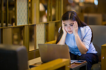 Woman using laptop in cafe at night time and she feel worried