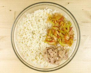 Making simple rice salad in a transparent bowl on wooden background - top view