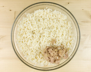 Making simple rice salad in a transparent bowl on wooden background - top view
