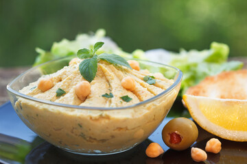 Homemade hummus with chickpeas, olive oil and mint leaf in glass bowl. Closeup of chickpeas and sesame humus.