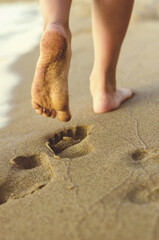 Girl walking on sand beach leaving footprints in the sand at sunset