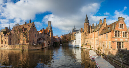 Naklejka na ściany i meble Morning Bruges,Belgium.Image In Realistic Color with Rozenhoedkaai in Brugge,Dijver river canal with Belfort (Belfry) tower.Flanders landmark.Panoramic scenic view with two white boats and cloudy sky
