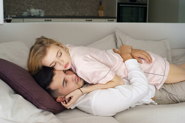 Young caucasian couple lying at sofa in living room at home, hugging and kissing on a sunny morning. Pretty blonde woman and brunette handsome man making love