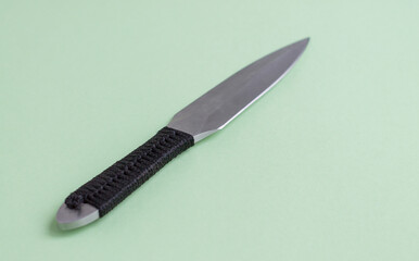 Knife for throwing with a black winding of a handle. On a light green background