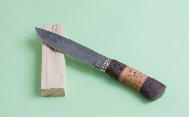 A knife made of Damascus steel. With a wooden handle. On a light green background