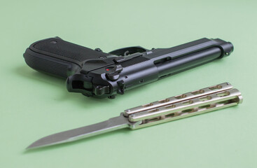 Black pistol and iron knife on a light green background