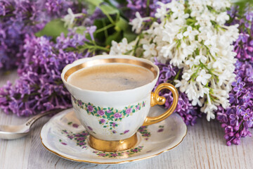 beautiful vintage cup of coffee and lilac flowers on light wooden table