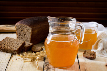 Traditional Russian cold rye drink Kvas in a glass and a jug on the kitchen table in a rustic style. Kvass from bread, rye malt, sugar and water. Copy space.
