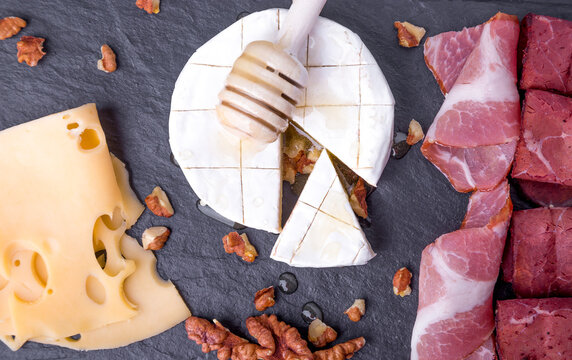 Cheese and meat plate with walnuts on black slate plate background. Top view. Camembert with honey