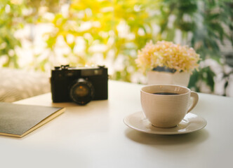 coffee cup, Retro camera, notebook and Plastic plants on white table in the coffeeshop the sun's rays in the morning