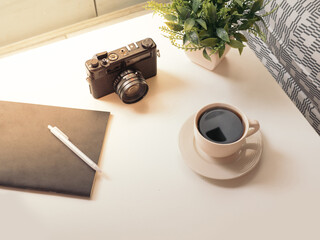coffee cup, Retro camera, notebook, white pen and green Plastic plants on white table in the coffeeshop with sun's rays in the morning