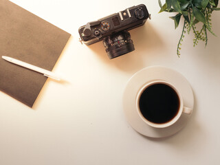 coffee cup, Retro camera, notebook, white pen and green Plastic plants on white table in the coffeeshop with sun's rays in the morning, top view