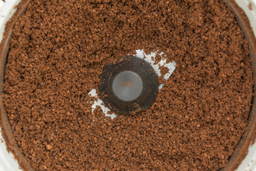 Ground grilled dark coffee beans in an automatic coffee grinder, close-up of food  background